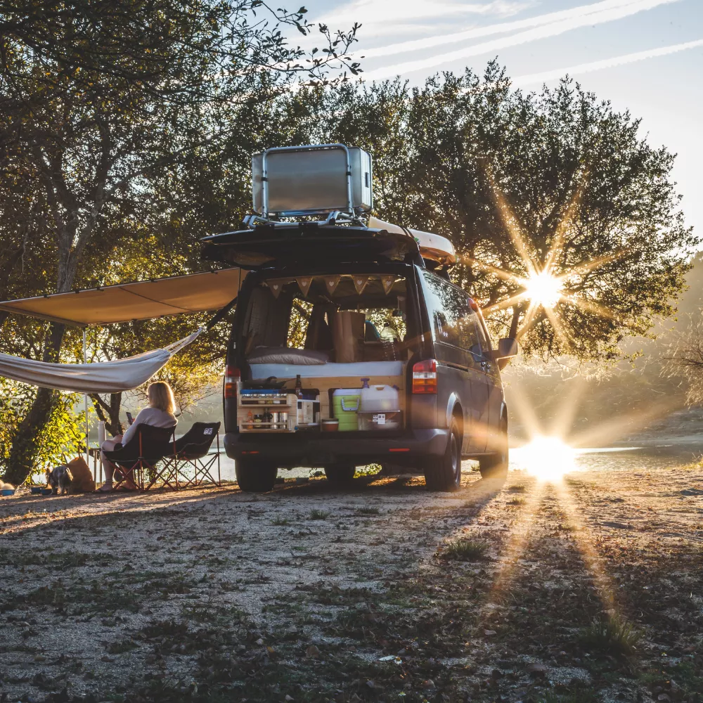 Camping-car aménagé au bord d'un lac au coucher du soleil, personne assise à côté