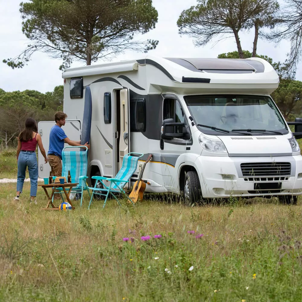Camping-car stationné dans un champ avec deux personnes et des chaises pliantes.