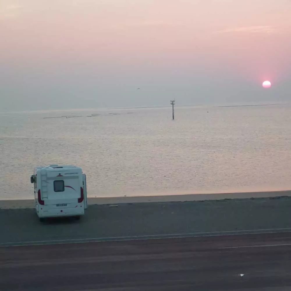 Camping-car stationné face à un coucher de soleil sur la mer
